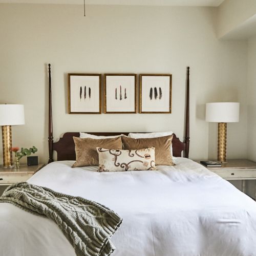A cozy bedroom with a king bed, white bedding, two matching nightstands, lamps, and framed art above the headboard.