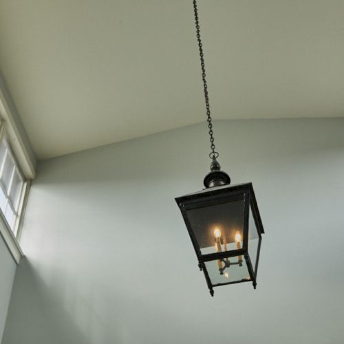 A hanging lantern fixture suspended by a chain from a high ceiling, flanked by tall windows and soft, pale walls.