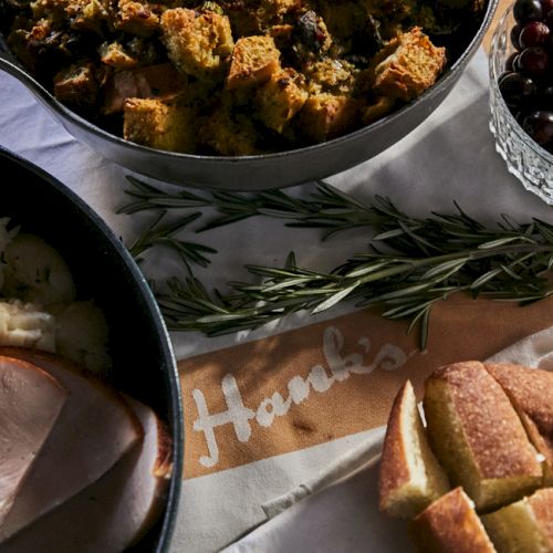 A cozy spread with sliced roasted meat, crusty bread, herbs, roasted veggies, and a bowl of berries on a dining table.